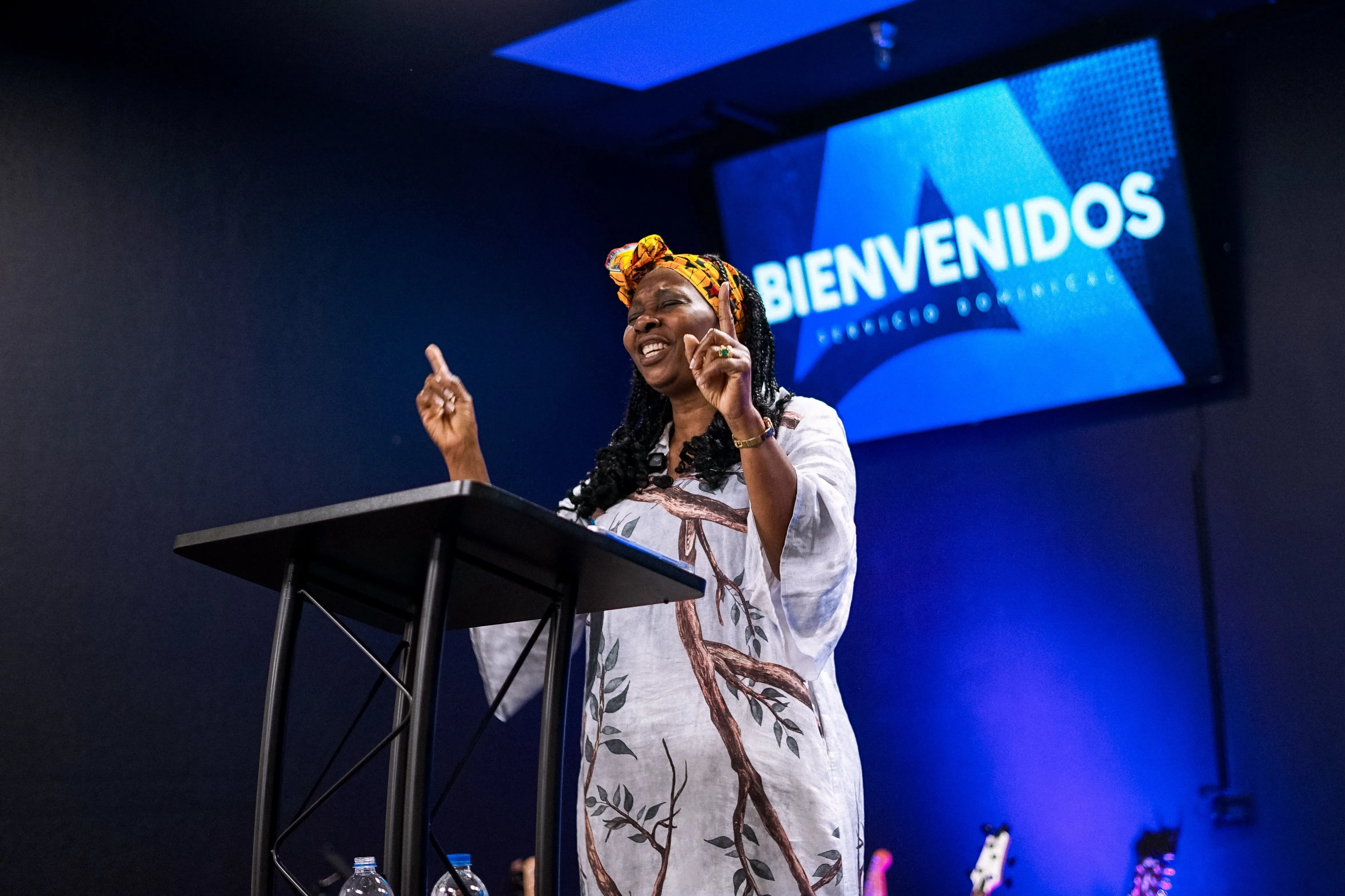 Una mujer predica desde el púlpito frente a la pantalla de Bienvenidos
